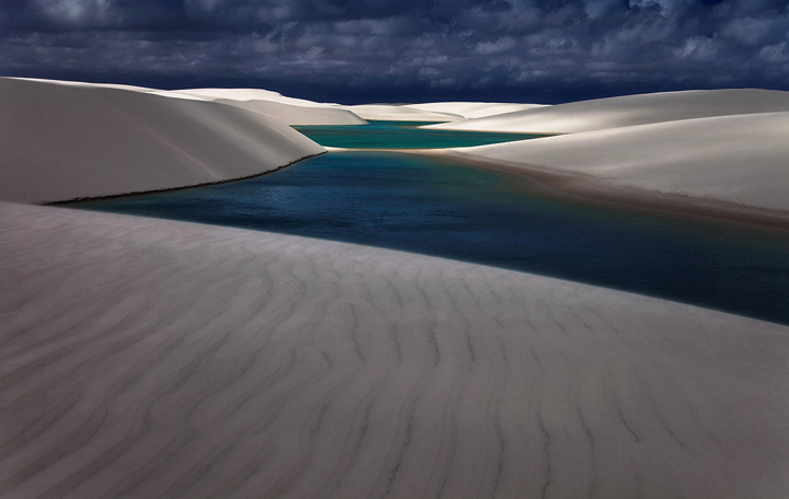 Tropical clouds race across the sky throwing light and shadows over the ridges and accenting the valleys of the vast dune field...