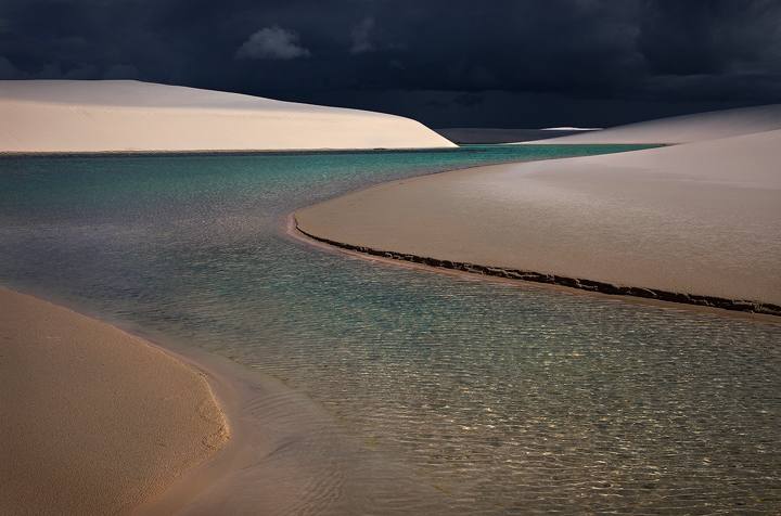 A powerful thunderstorm darkens the sky over the dunes of Lencois Maranhenses National Park. I spent three days trekking barefoot...