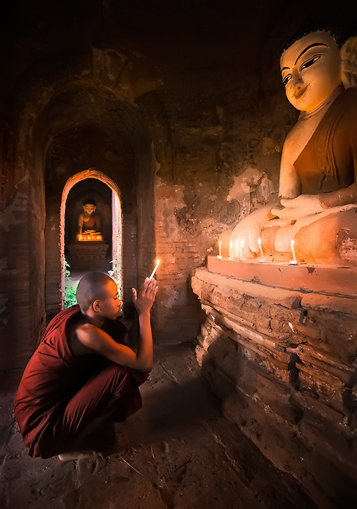 A young monk prays before an ancient Buddha in Bagan, Burma.