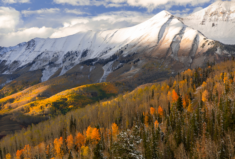 October snow blankets the summit crest of Mt Campbell and the San Sofia range as sunset light streams into the autumn forest...