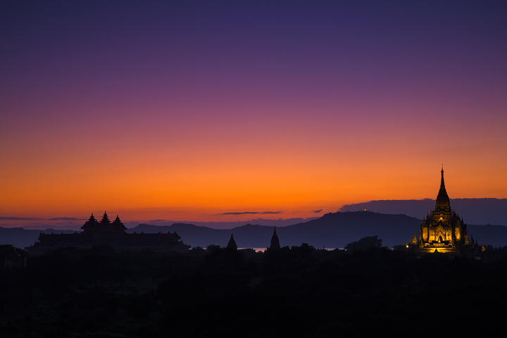 Twilight fades over the ancient riverside temples of Bagan, Burma. The lighted temple on the summit of Mt Popa can be seen in...